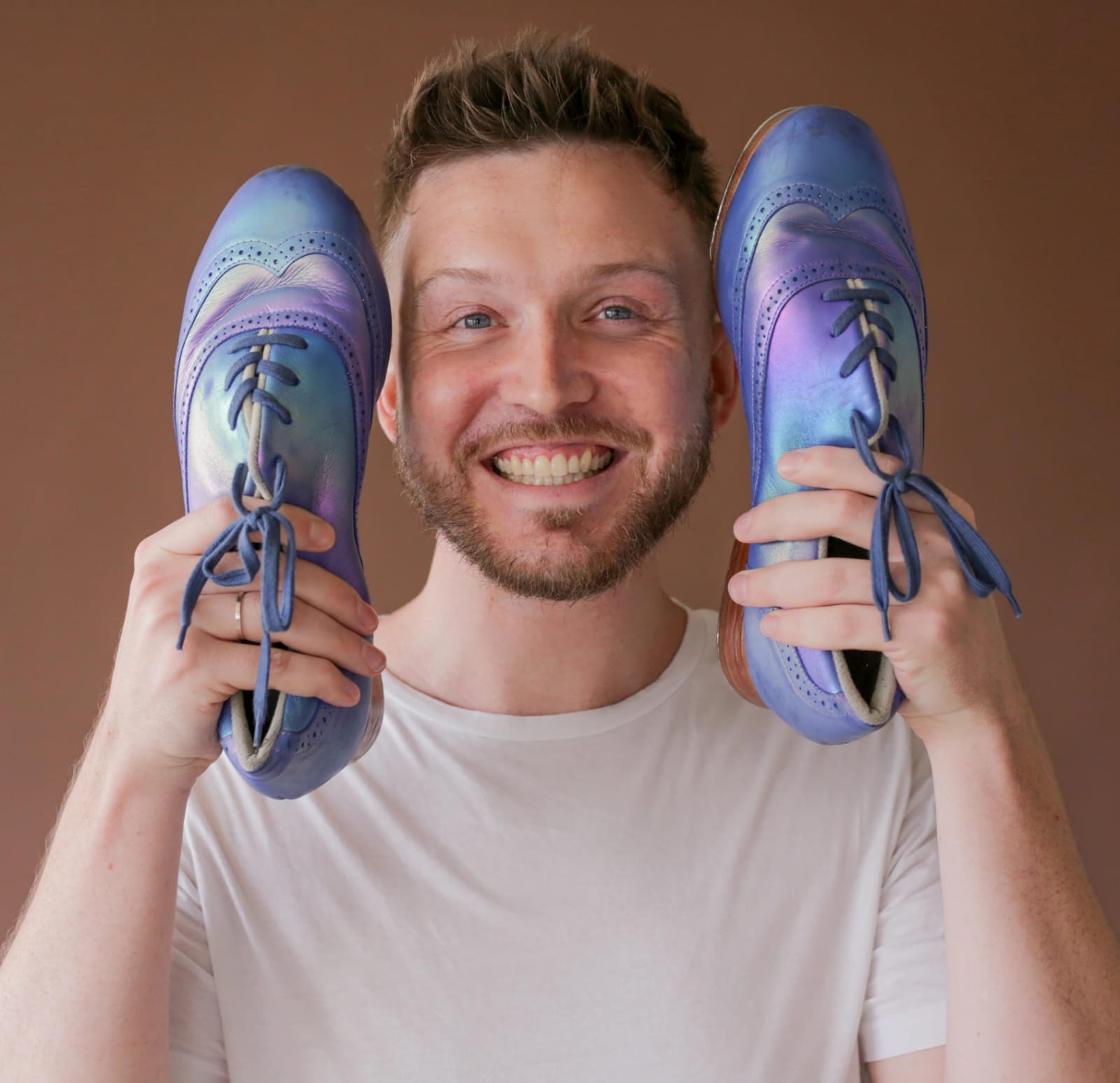 Colby D. Adams sorrindo e segurando um par de sapatos de sapateado azuis ao lado do rosto