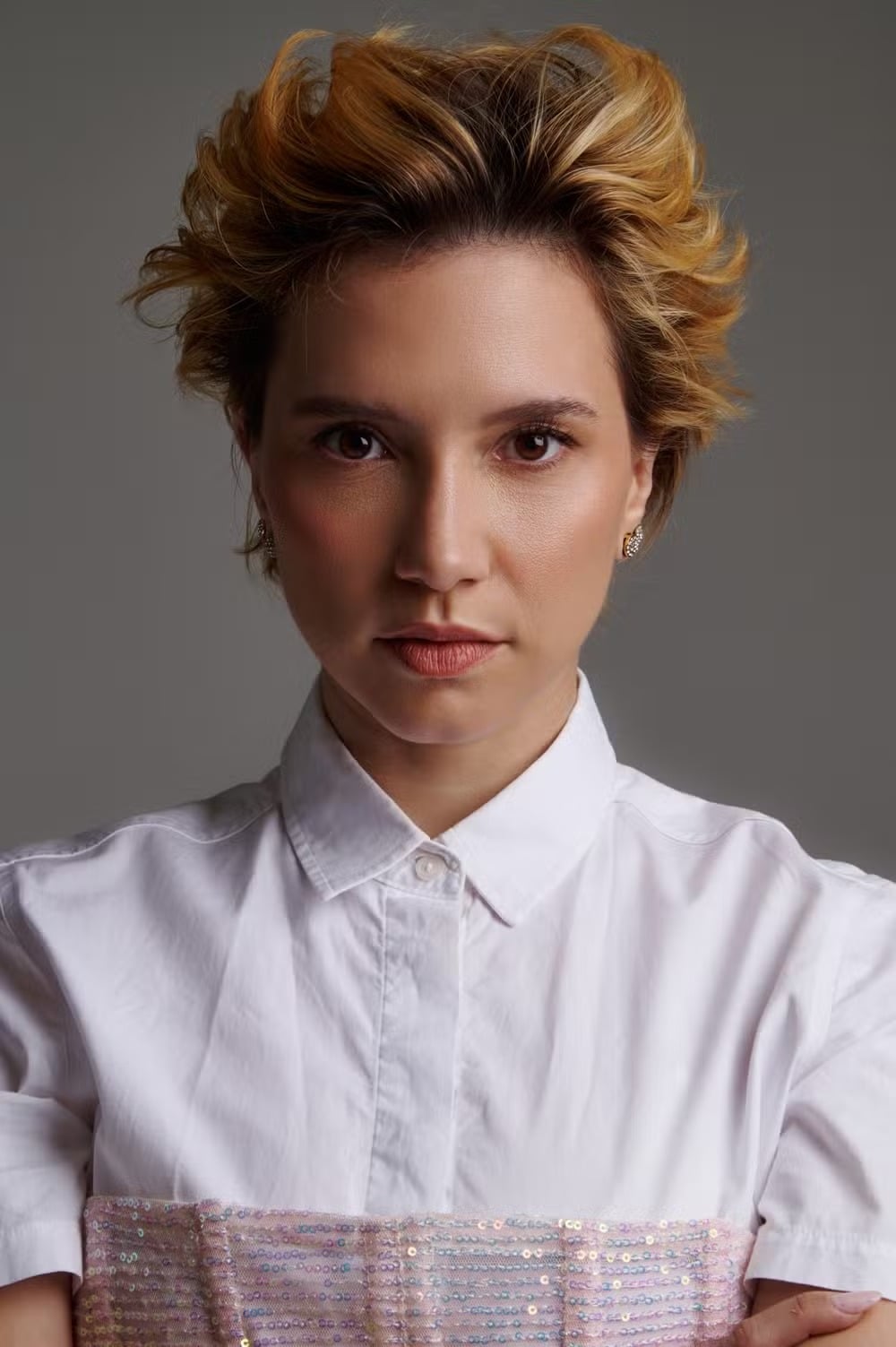 Retrato de Lorena Comparato, de cabelo curto e camisa branca, sobre fundo cinza